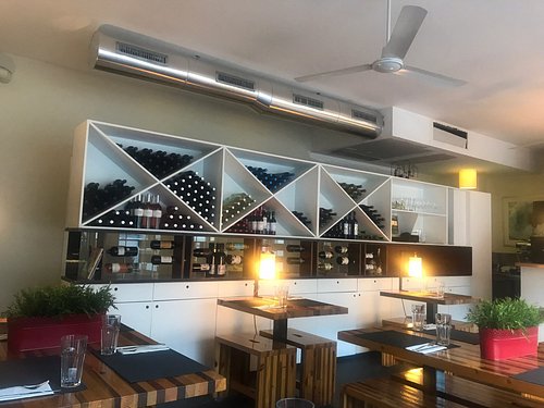 Sala de refeições da Presto Pizza em Matosinhos com mesas de madeira às riscas e uma estante branca de vinhos